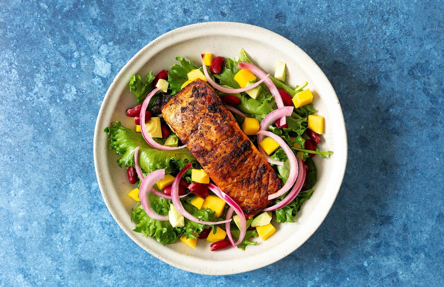 Pan-seared jerk salmon over mixed greens with pickled red onions, mango and avocado.